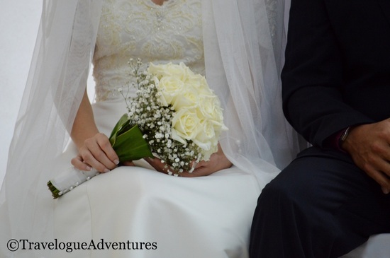 A bride in a white gown holding a bouquet of white flowers next to a groom in a black suit.