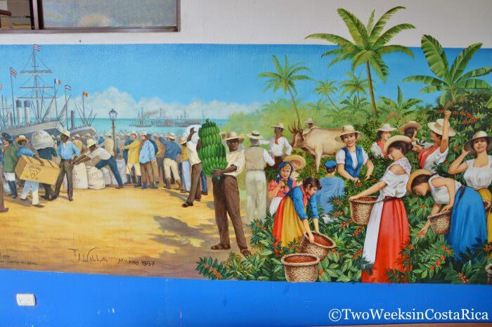 A wall mural showing people lined up in a tropical setting holding coffee and bananas, ready to load their goods onto waiting boats
