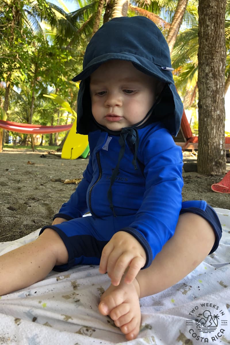 a baby at the beach wearing a full coverage bathing suit and hat