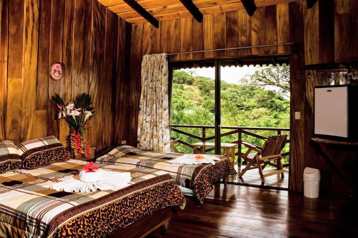 a wooden hotel room with two beds and a porch looking out to the forest