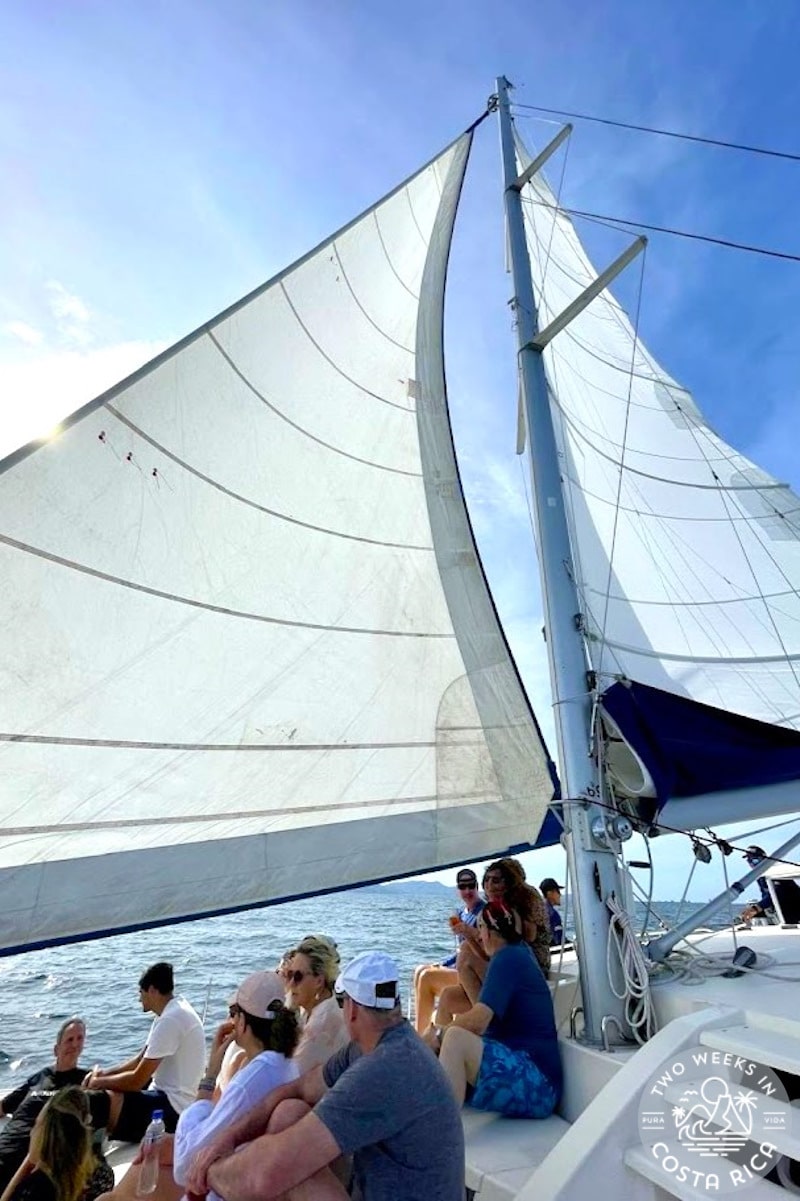 people sitting on a boat with the sails up