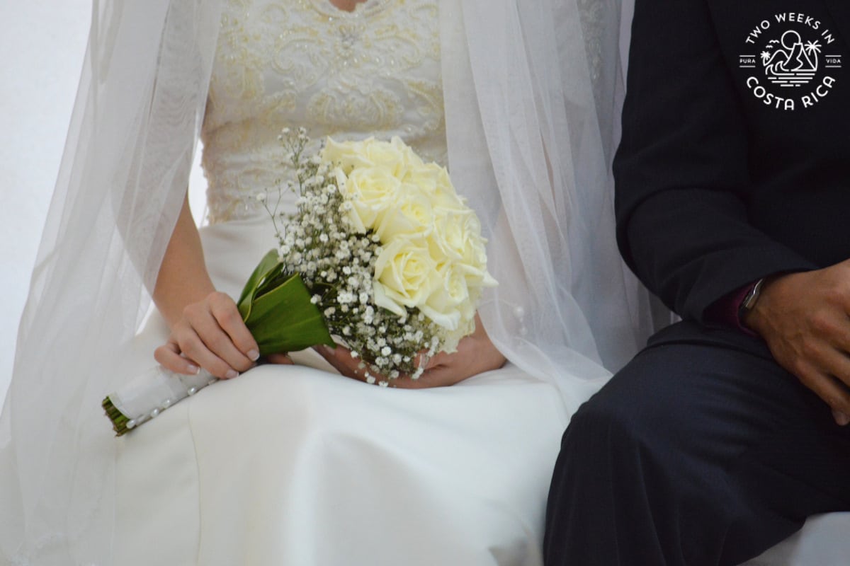 A bride in a white dress holding a bouquet of flowers next to a groom in a black suit