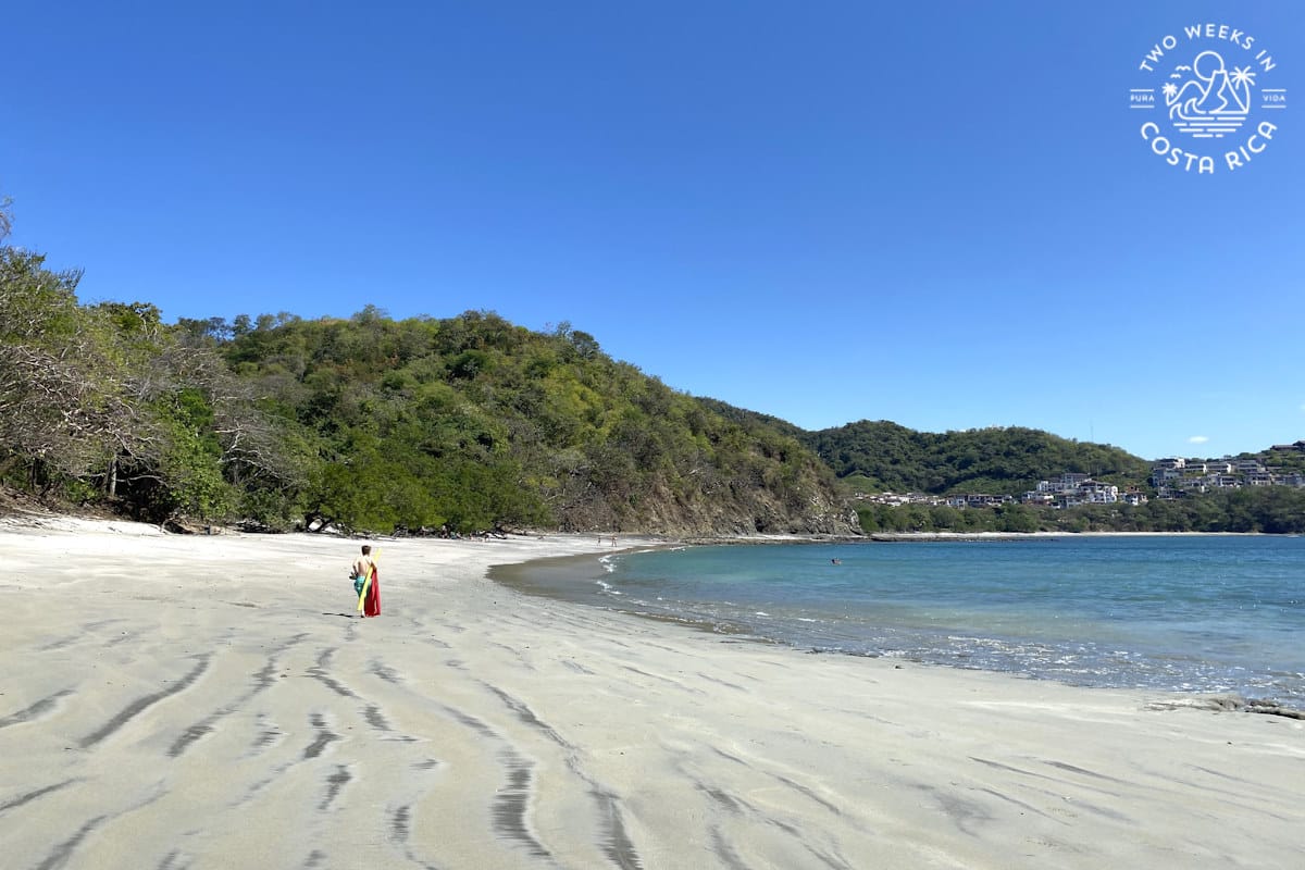 a person walking on the white sand beach at dantita beach with blue sky