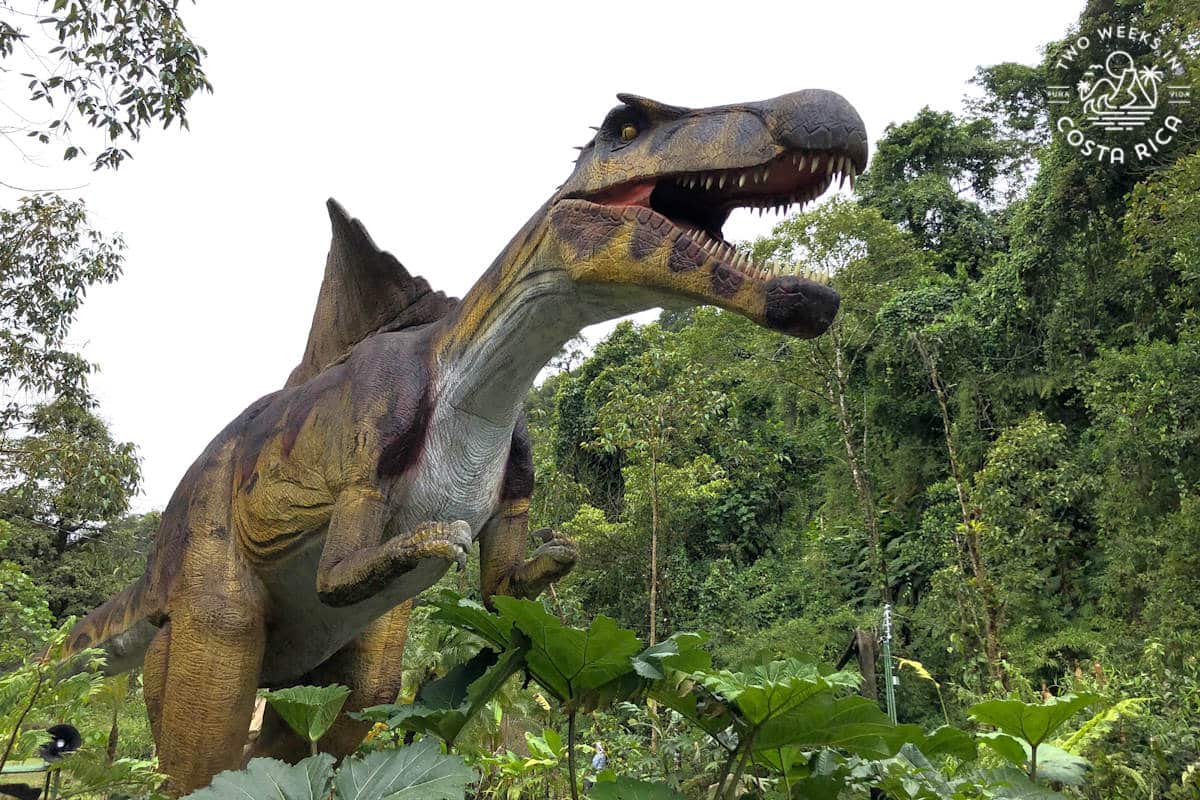 a huge T Rex statue outside with thick jungle all around