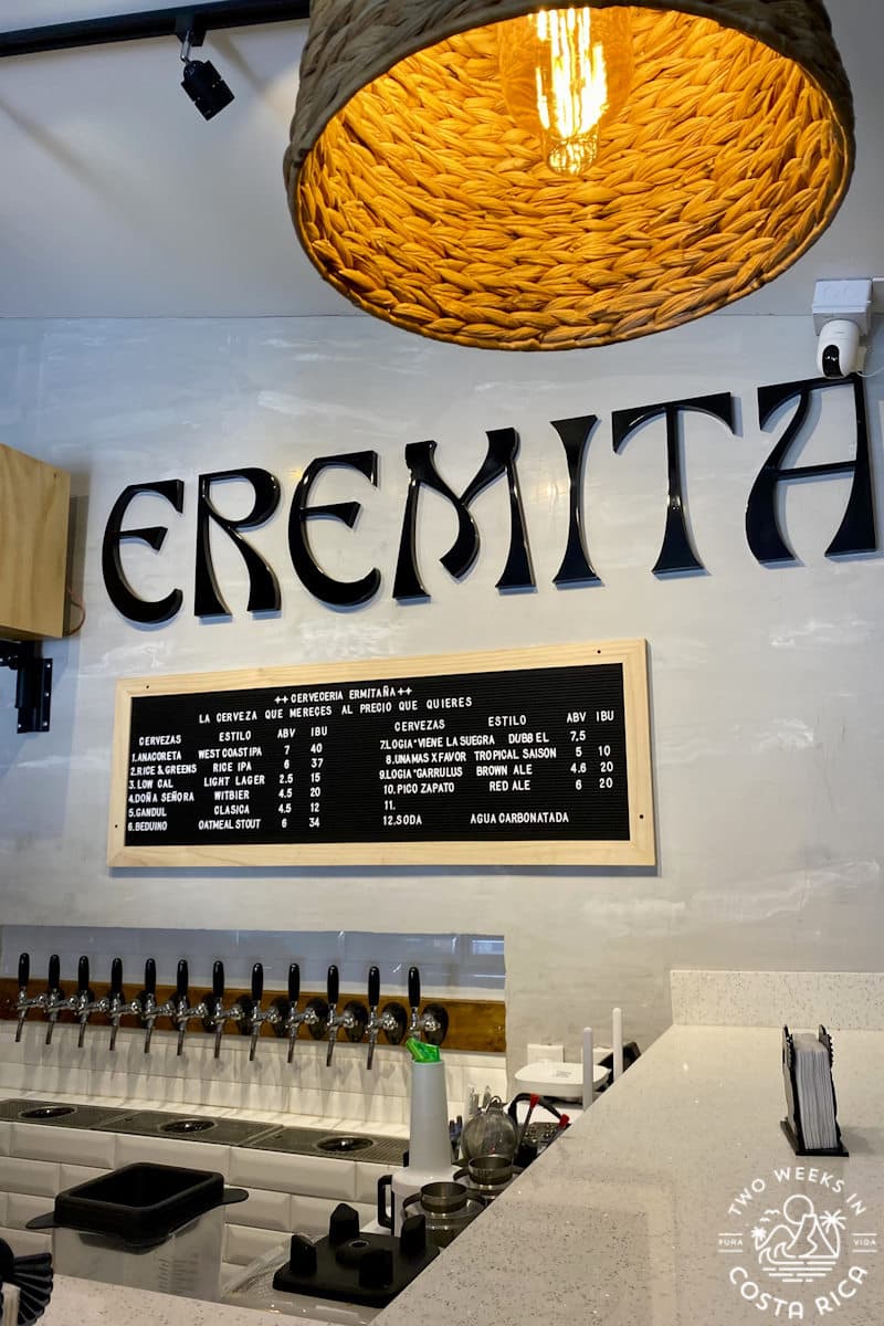Row of taps set along a white tile wall with large black letters spelling EREMITA above