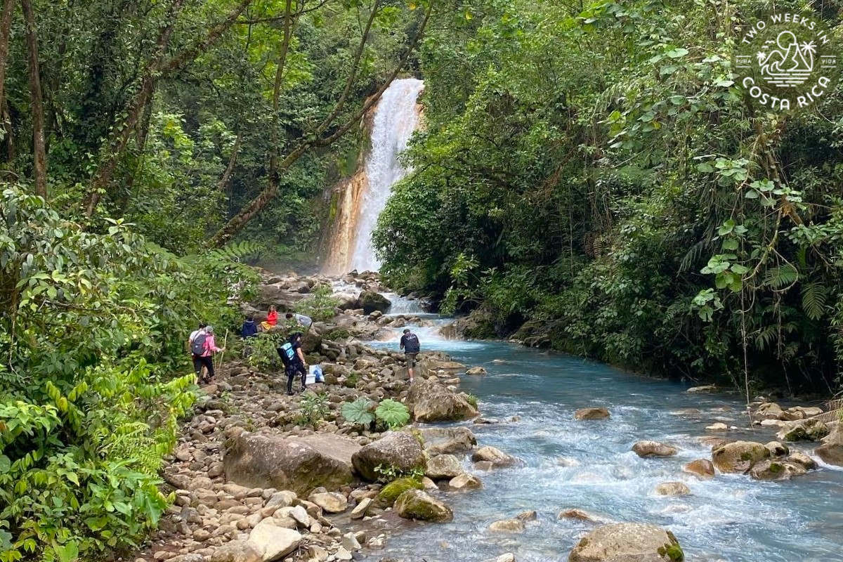 Hikers trekking next to a blue river to get to a waterfall in Costa Rica