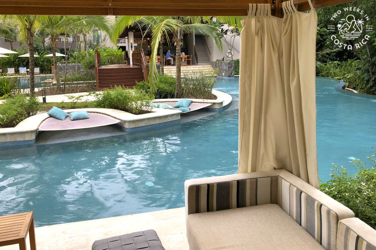 a poolside cabana with tropical plants and palm trees in the background