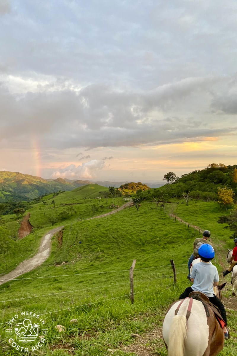 people on a horseback riding tour in monteverde with views of green mountains and a rainbow