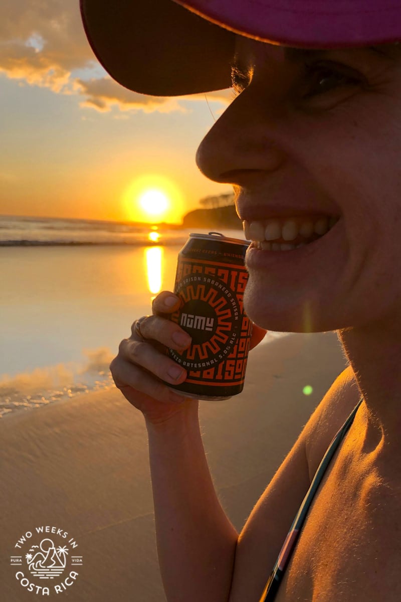 One of the owners of the website Two Weeks in Costa Rica holding a beer on the beach at sunset
