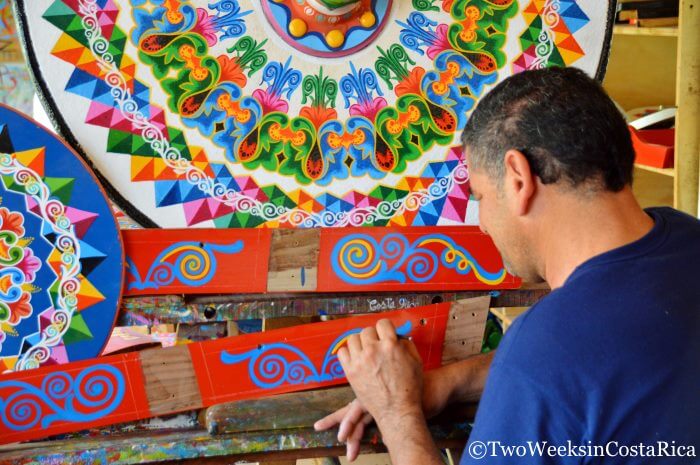 An artist painting decorations on parts of an oxcart 