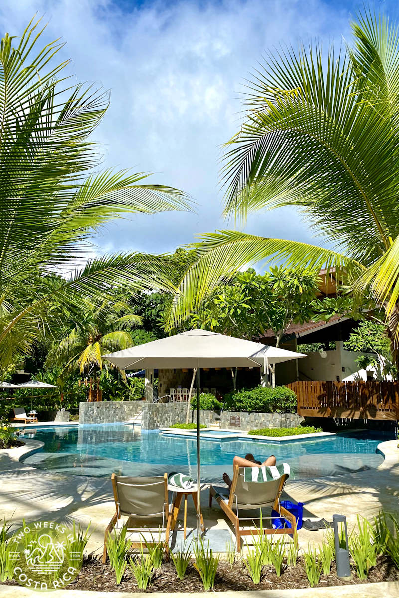 someone sitting under an umbrella in a lounge chair next to a pool