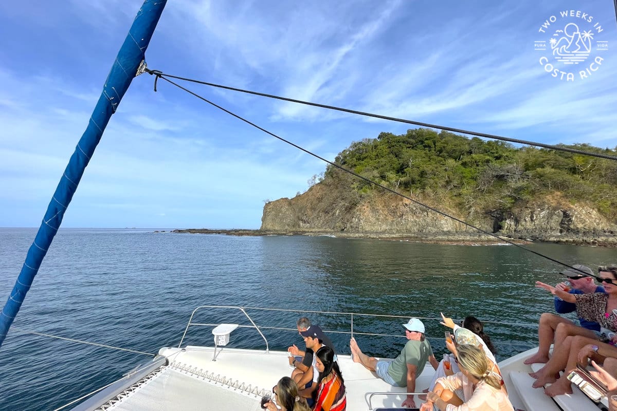 people sitting on the front of a boat in the ocean with an island in the background