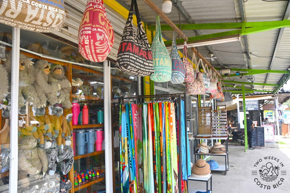 open stores along a sidewalk with bags, sarongs, and souvenirs