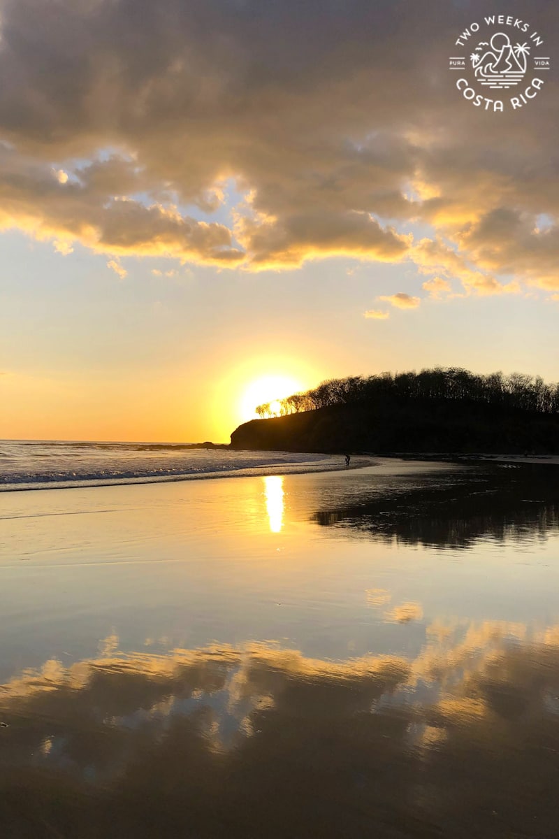 an orange sunset going behind a point along the ocean