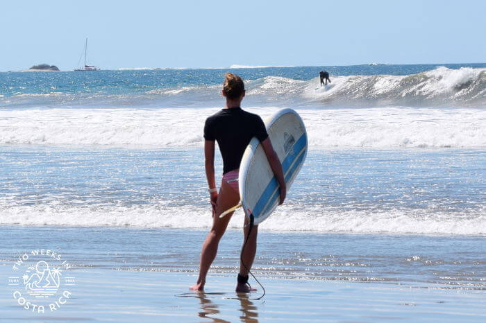 A woman holding a surf board and looking at the waves at Playa Grande