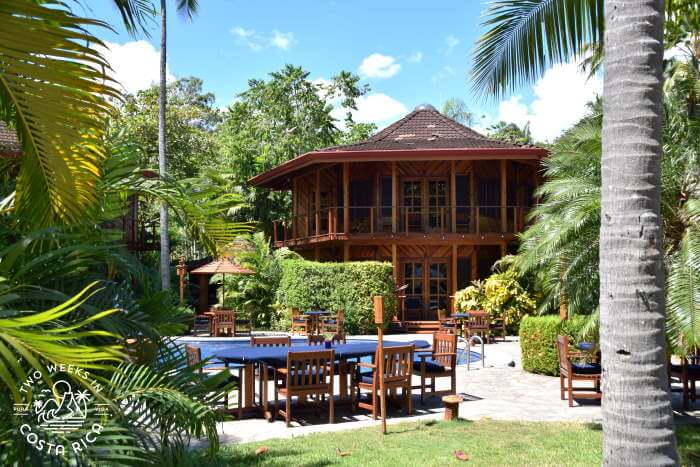 A wooden hotel building, tables, and a pool at Tambor Tropical Beach Resort