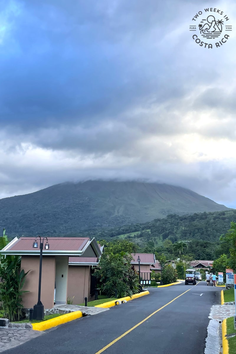 clouds covering the top of a volcano with small buildings and a road in the foreground